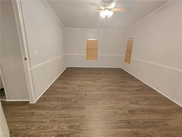 Empty room featuring dark wood-style flooring, ornamental molding, and a ceiling fan
