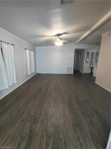 Unfurnished living room featuring dark wood-type flooring, crown molding, and ceiling fan