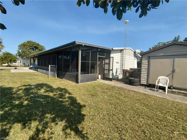 Rear view of property with a sunroom, a lawn, and a storage unit
