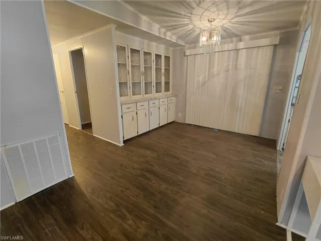 Unfurnished dining area featuring dark wood-type flooring, a chandelier, and crown molding