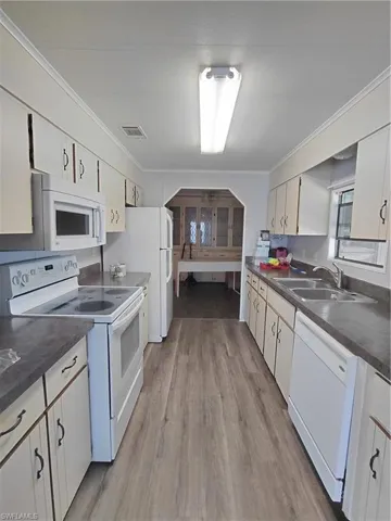 Kitchen with white appliances, dark countertops, crown molding, light wood finished floors, and white cabinets