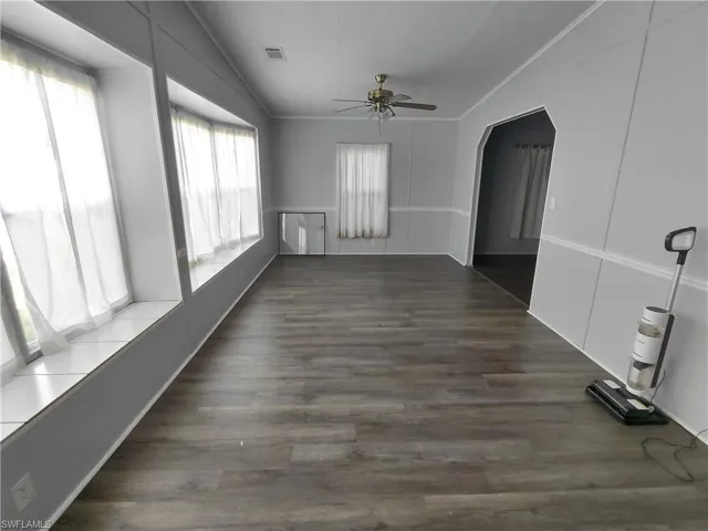 Empty room featuring arched walkways, ceiling fan, crown molding, dark wood finished floors, and a decorative wall