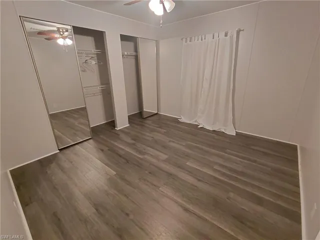 Unfurnished bedroom with wood finished floors, two closets, and a ceiling fan