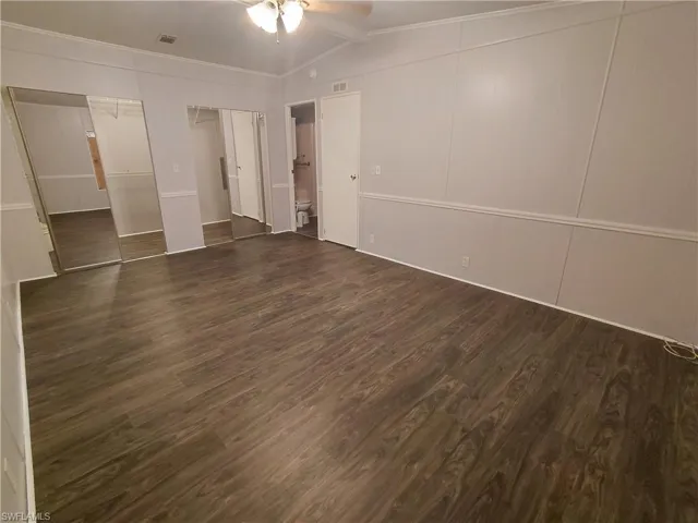 Unfurnished bedroom with dark wood-type flooring, ornamental molding, lofted ceiling, ceiling fan, and two closets