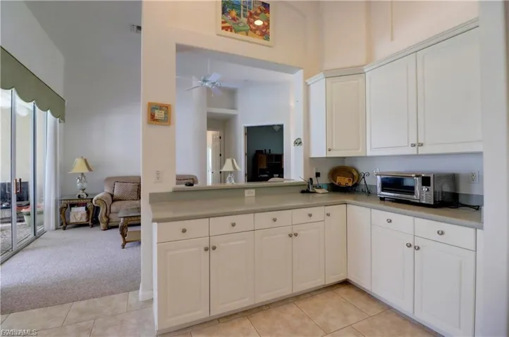 Kitchen with light countertops, light carpet, white cabinets, ceiling fan, and a high ceiling