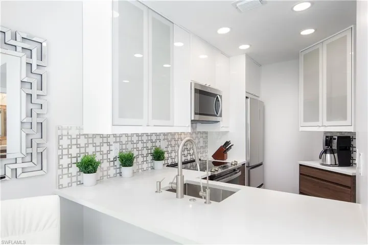 Contemporary kitchen featuring white cabinetry, stainless steel appliances, a geometric tile backsplash, recessed lighting, and white countertops
