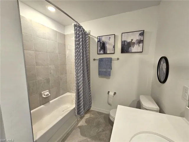 Bathroom with toilet, shower / bath combo with shower curtain, and baseboards