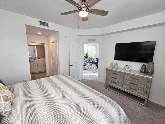 Bedroom with ensuite bath, visible vents, ceiling fan, and carpet flooring