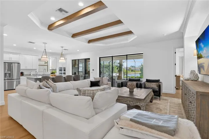 Living room with ornamental molding, light wood-style floors, beam ceiling, a raised ceiling, and recessed lighting