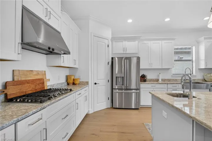 Kitchen featuring white cabinets, stainless steel appliances, light stone countertops, recessed lighting, and ornamental molding