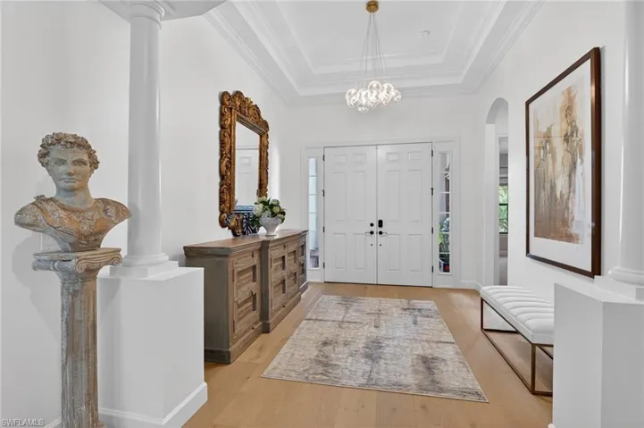 Entrance foyer with a raised ceiling, wood finished floors, hanging lights, crown molding, and arched walkways
