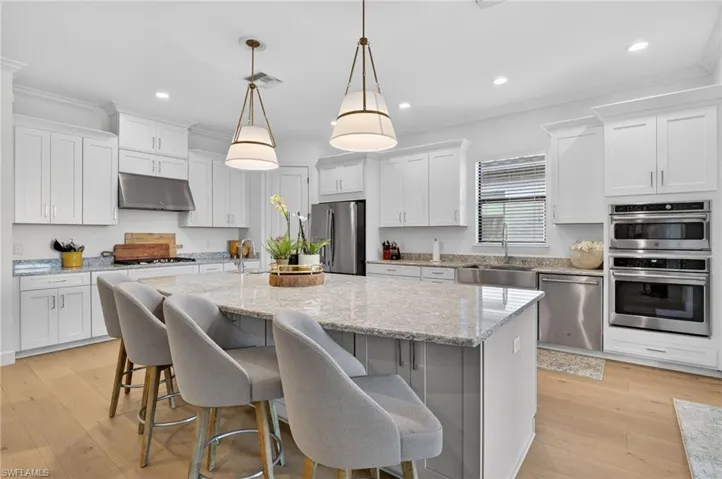 Kitchen featuring a center island with sink, light stone countertops, white cabinets, a breakfast bar area, and crown molding