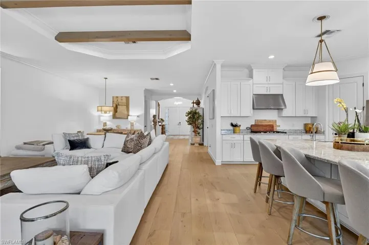 Living area featuring crown molding, arched walkways, light wood-style flooring, recessed lighting, and beamed ceiling