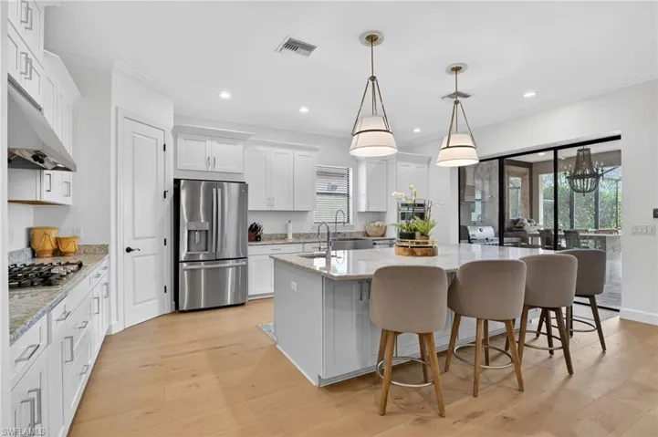 Kitchen with white cabinets, a center island with sink, light stone countertops, a kitchen breakfast bar, and crown molding