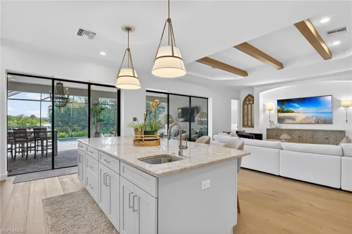 Kitchen featuring light stone countertops, decorative light fixtures, light wood-style flooring, an island with sink, and open floor plan