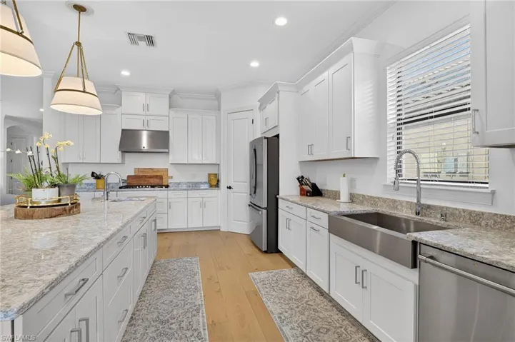 Kitchen featuring white cabinets, stainless steel appliances, light stone countertops, and ornamental molding