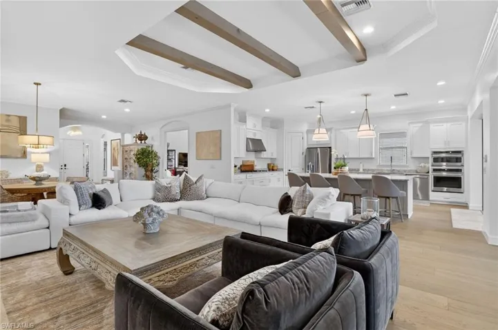 Living room featuring arched walkways, crown molding, recessed lighting, light wood-style floors, and beamed ceiling