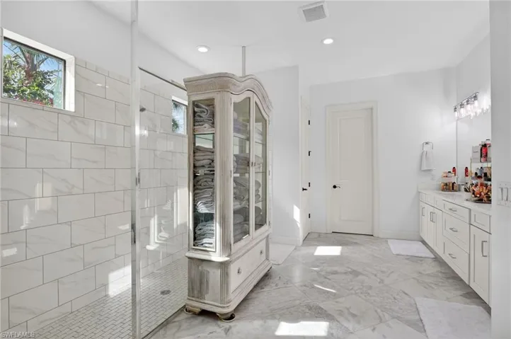 Bathroom featuring walk in shower, vanity, light marble finish floors, and recessed lighting