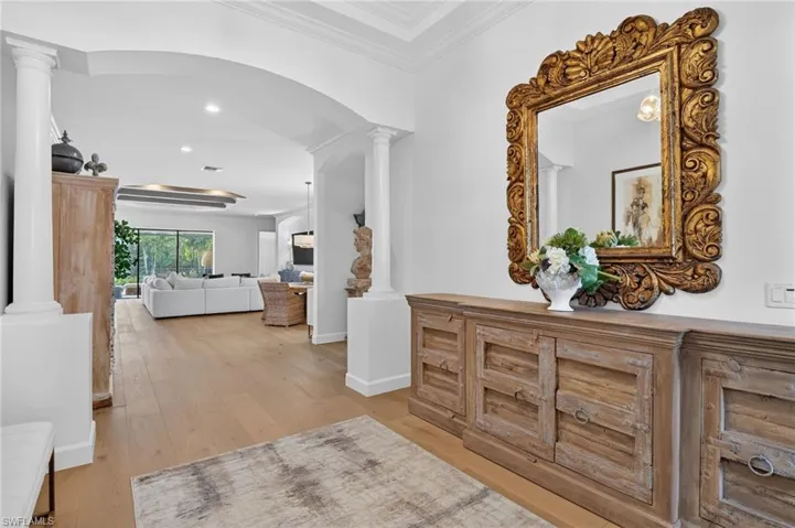 Corridor featuring decorative columns, light wood finished floors, recessed lighting, ornamental molding, and arched walkways