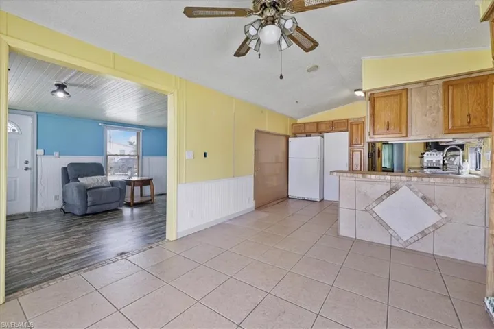 Kitchen featuring light tile patterned floors, a textured ceiling, freestanding refrigerator, open floor plan, and a wainscoted wall