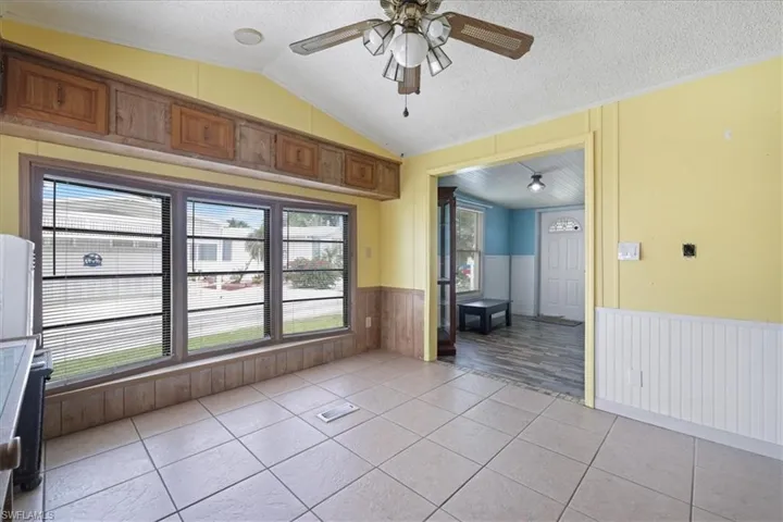 Unfurnished room with a wainscoted wall, a textured ceiling, vaulted ceiling, light tile patterned flooring, and ceiling fan