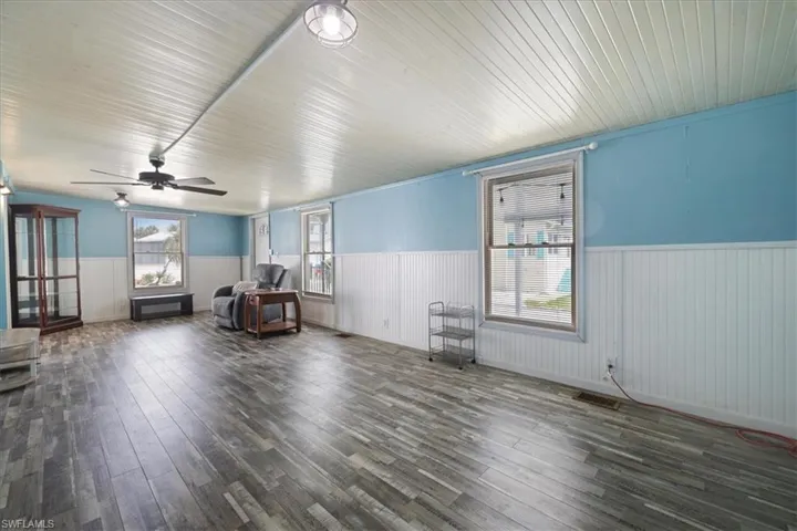 Living area with a wainscoted wall, dark wood-style floors, healthy amount of natural light, and a ceiling fan