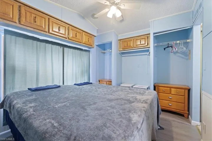 Bedroom with crown molding, light wood-type flooring, lofted ceiling, a textured ceiling, and ceiling fan