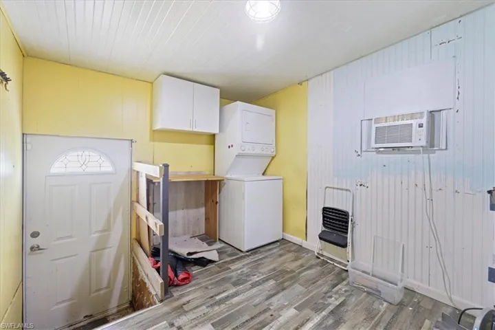 Laundry room featuring wood walls, stacked washer / drying machine, wood finished floors, and cabinet space