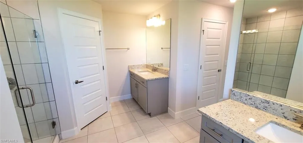 Primary Bathroom featuring a shower with door, vanity, and tile patterned flooring