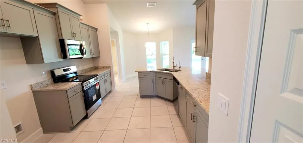 Kitchen with sink, light stone countertops, hanging light fixtures, appliances with stainless steel finishes, and light tile patterned flooring