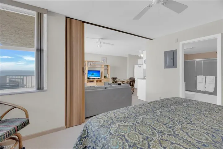 Bedroom featuring electric panel, light colored carpet, freestanding refrigerator, ceiling fan, and a water view