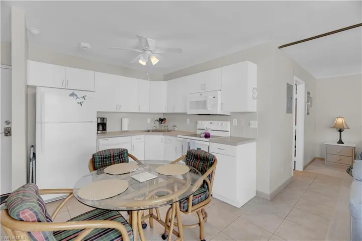 Kitchen featuring white appliances, light countertops, decorative backsplash, light tile patterned floors, and white cabinets