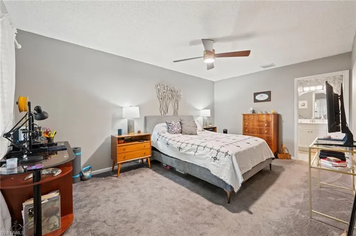 Carpeted bedroom featuring ceiling fan, ensuite bathroom, and a textured ceiling
