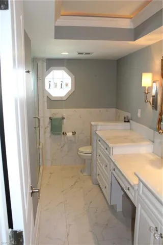 Bathroom with vanity, a marble finish shower, light marble finish flooring, ornamental molding, and wainscoting