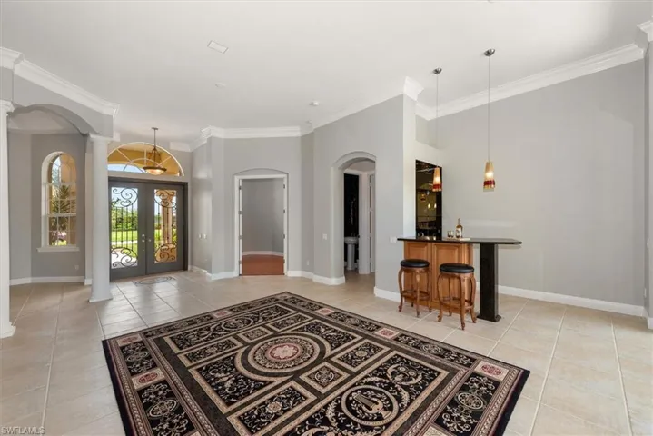 Entryway featuring decorative columns, arched walkways, light tile patterned flooring, crown molding, and bar