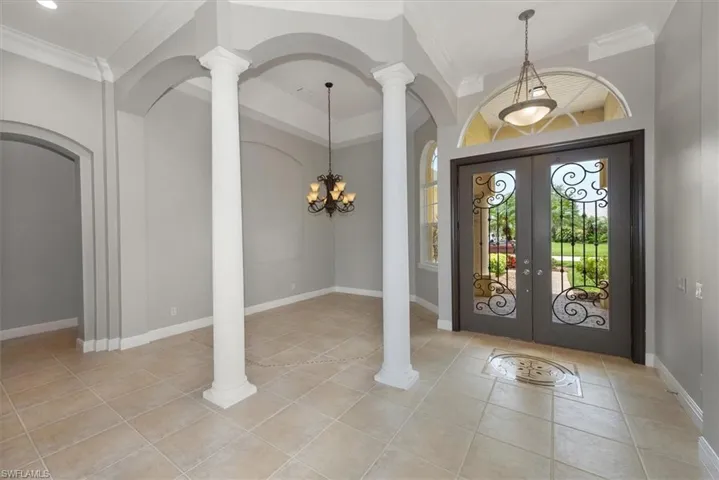 Foyer featuring decorative columns, french doors, light tile patterned floors, arched walkways, and crown molding