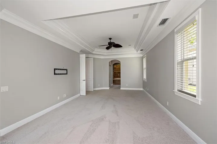 Empty room with arched walkways, crown molding, a ceiling fan, a raised ceiling, and light carpet