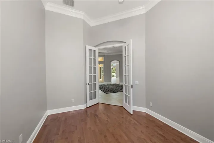 Unfurnished room with french doors, arched walkways, ornamental molding, and wood finished floors