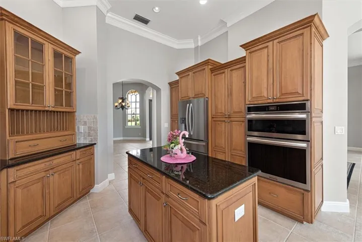 Kitchen with stainless steel appliances, arched walkways, light tile patterned floors, ornamental molding, and dark stone counters