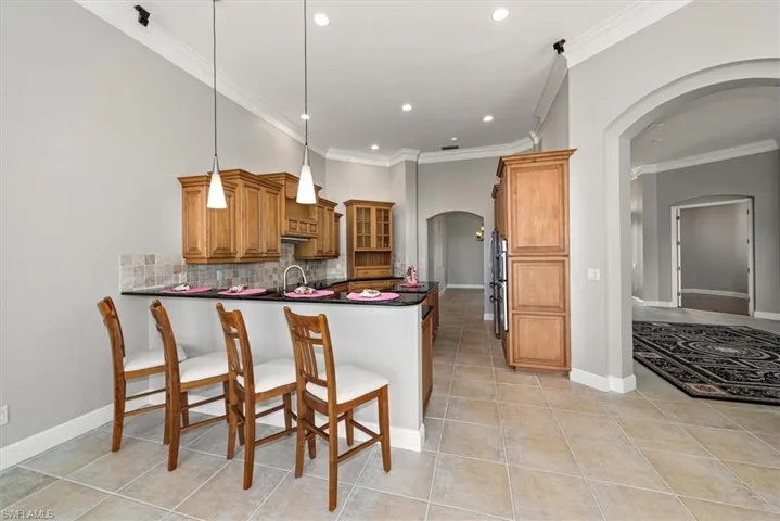 Kitchen with arched walkways, crown molding, a peninsula, brown cabinetry, and light tile patterned flooring