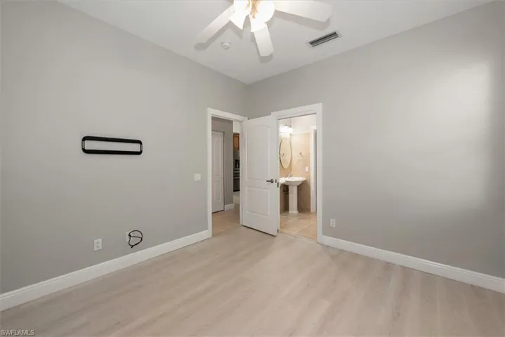 Unfurnished bedroom with light wood-type flooring, connected bathroom, and ceiling fan