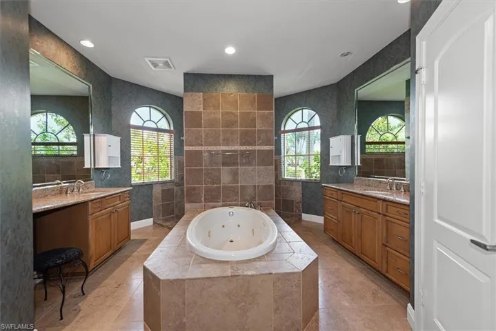 Full bathroom featuring a tub with jets, two vanities, recessed lighting, and tile walls