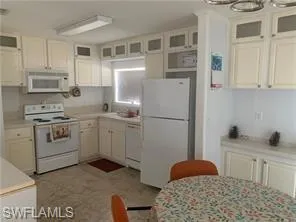 Kitchen featuring white appliances, light countertops, glass insert cabinets, and white cabinets