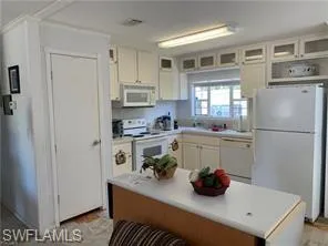 Kitchen featuring glass insert cabinets, white appliances, light countertops, and white cabinetry