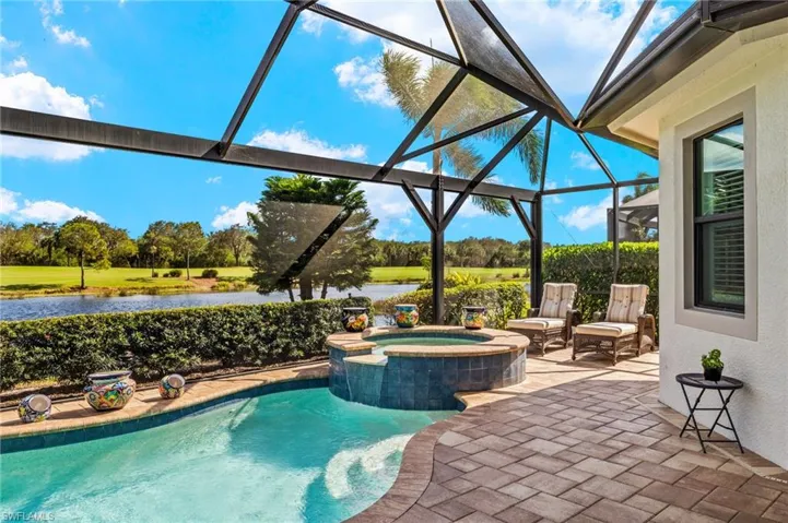 View of pool with an in ground hot tub, a patio, a water view, and glass enclosure
