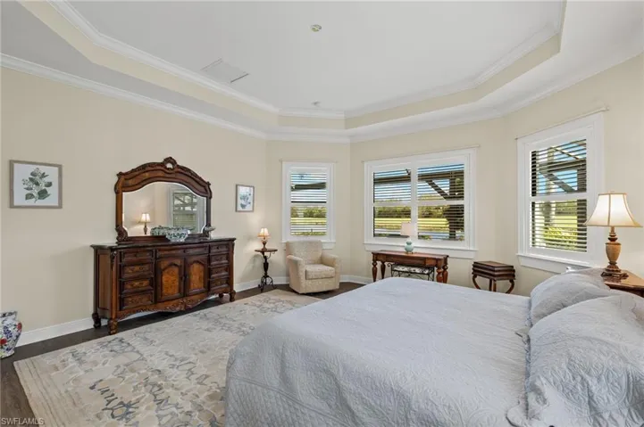 Bedroom with dark hardwood / wood-style floors, a raised ceiling, multiple windows, and crown molding