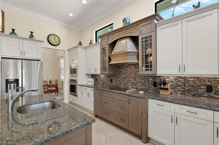 Kitchen featuring white cabinets, stainless steel appliances, ornamental molding, and dark stone countertops