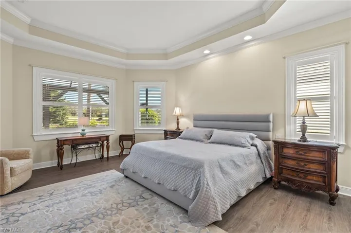 Bedroom with wood-type flooring, a raised ceiling, and ornamental molding