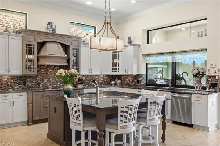 Kitchen featuring dark stone countertops, a center island with sink, stainless steel dishwasher, and decorative light fixtures