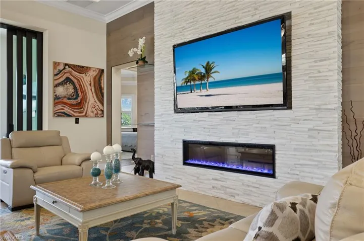 Tiled living room featuring crown molding and a stone fireplace